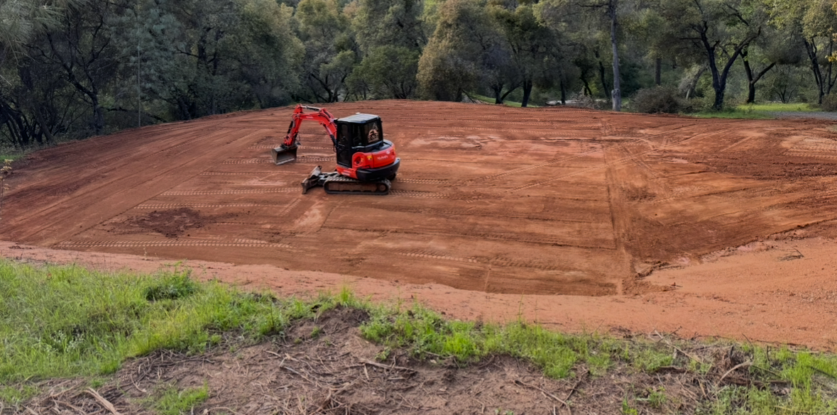 A red excavator is moving dirt in a field.