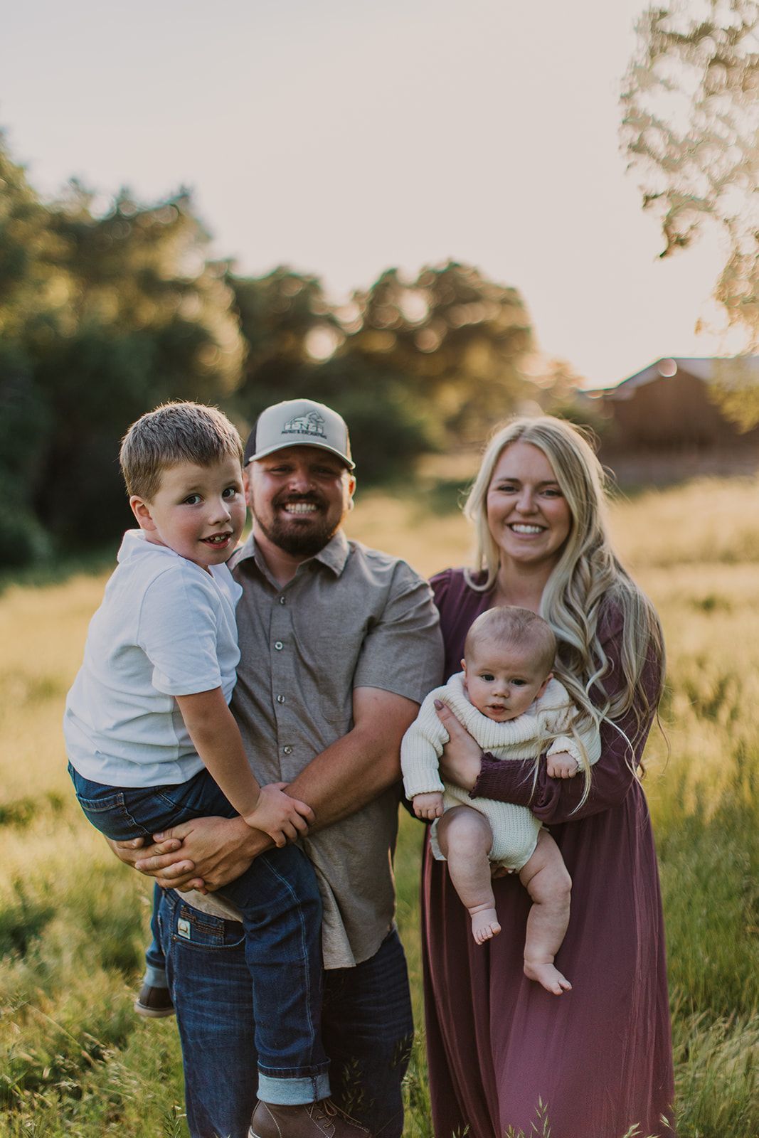 Family of four standing outdoors at sunset, with two adults holding two young children.