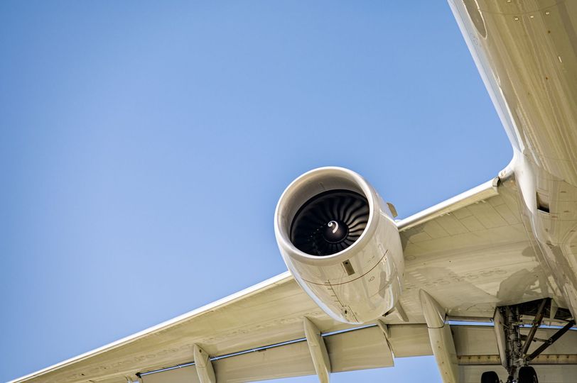 A close-up of a white airplane wing and jet engine against a clear blue sky.