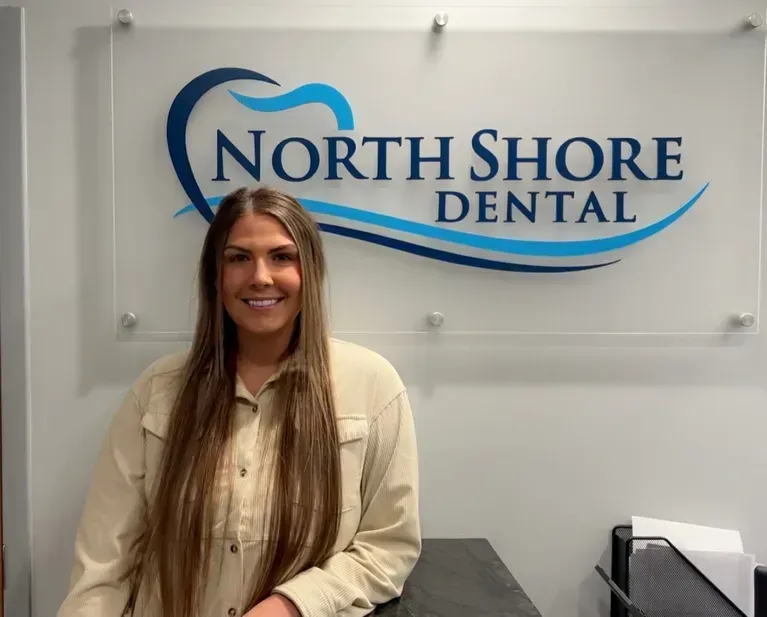 Woman standing in front of a North Shore Dental sign, smiling in an office lobby.