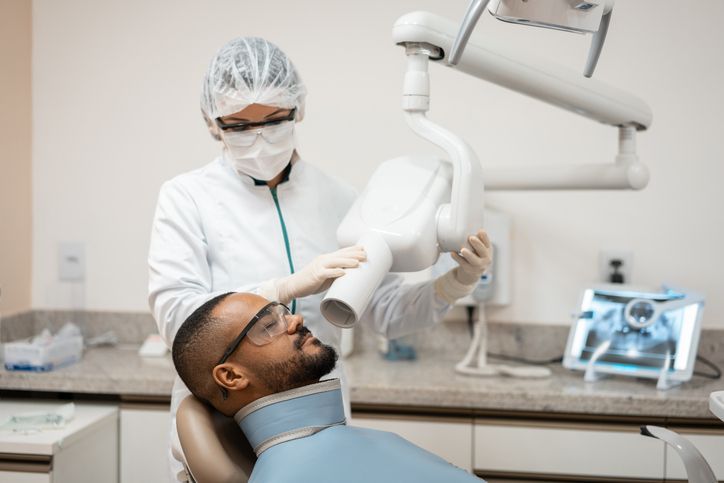Dentist in white protective gear examining a patient in a dental chair with a dental tool