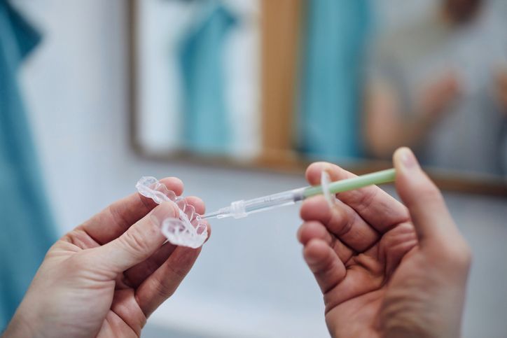 Hands drawing liquid into a syringe from a small glass vial against a blurred blue background