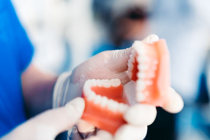 Gloved hands holding a set of dental prosthetic teeth in a clinical setting