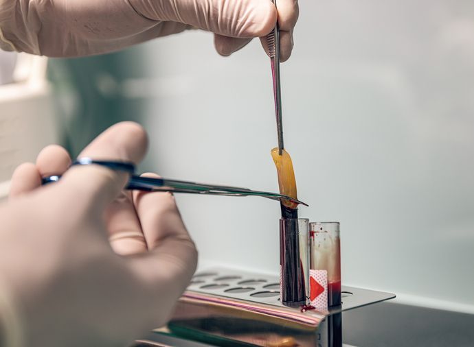 Hands using tweezers and a brush to apply orange paint to a small glass container