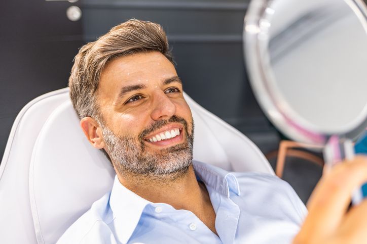 Smiling man reclining in a dental chair, looking into a handheld mirror