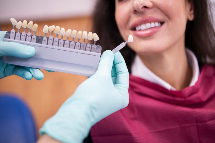 Dentist showing tooth shade samples to a smiling patient wearing a maroon scarf