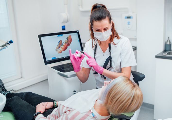 Dentist in pink gloves examining a patient in a dental chair beside a monitor