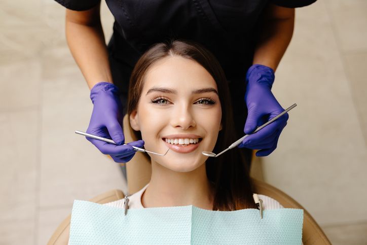 Woman smiling during dental exam as clinician adjusts her mouth with gloved hands and tools