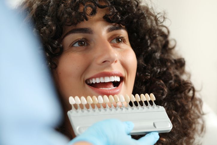 Smiling person choosing tooth shade with dental shade guide in a clinic