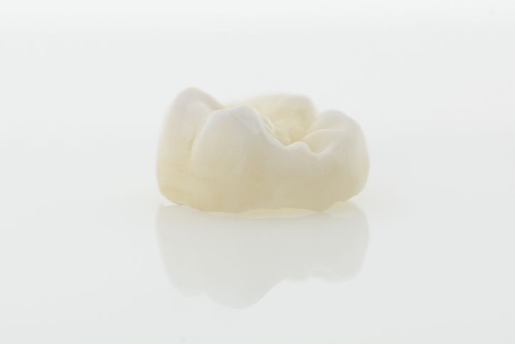 A single white tooth on a white background with a faint reflection