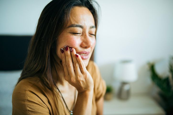 Woman smiling with eyes closed and hands on her cheeks in a bright indoor setting
