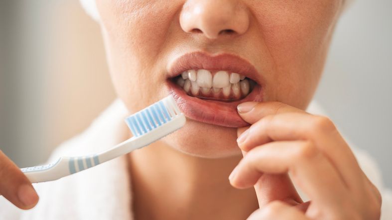 Person brushing lower teeth with a blue toothbrush while flossing in a close-up bathroom scene