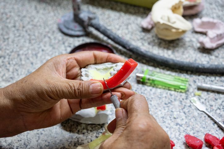 Hands shaping red clay around a white mold on a speckled worktable, with sculpting tools nearby