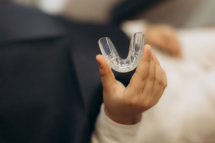 Hand holding a clear U-shaped dental aligner against a blurred indoor background