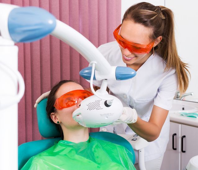 Dentist using a teeth-whitening light on a patient in a dental chair