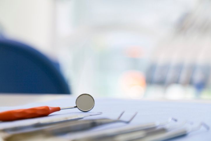 Dental mirror and tools on a white tabletop, with a blurred blue chair in the background