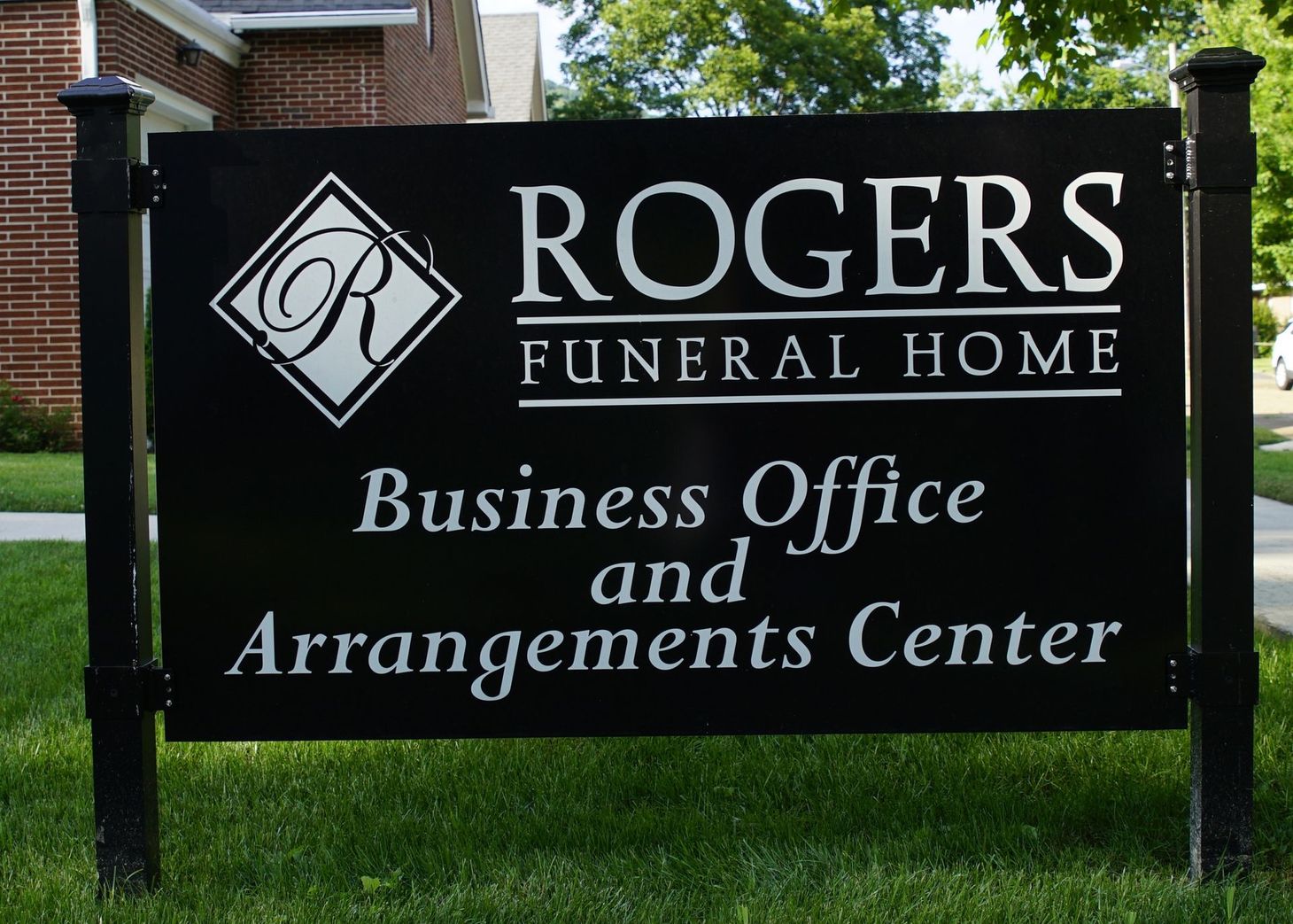 Sign for Rogers Funeral Home, black with white text, on a green lawn. "Business Office and Arrangements Center" is below.