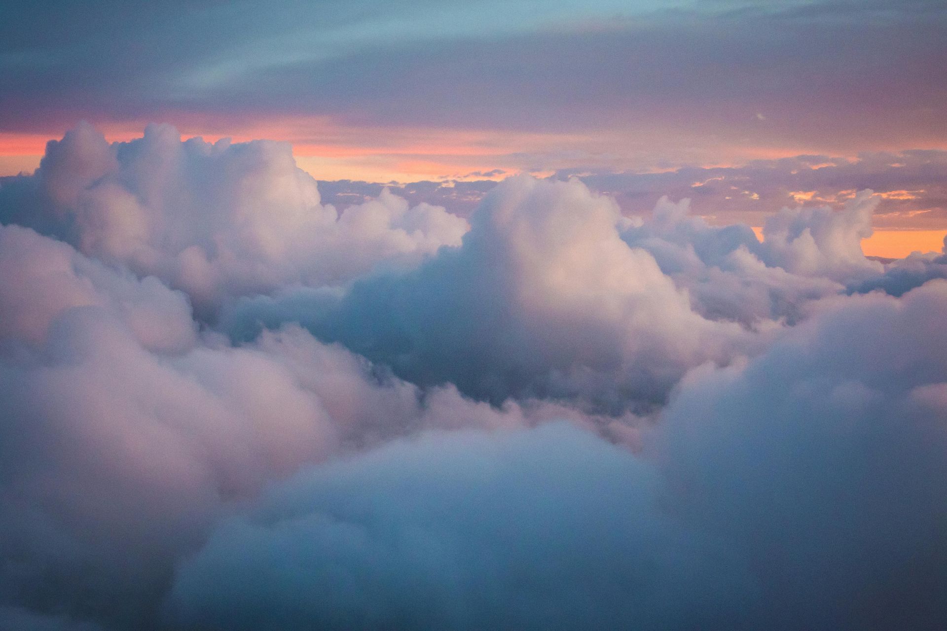 Clouds bathed in pink and orange hues at sunset, blue sky above.