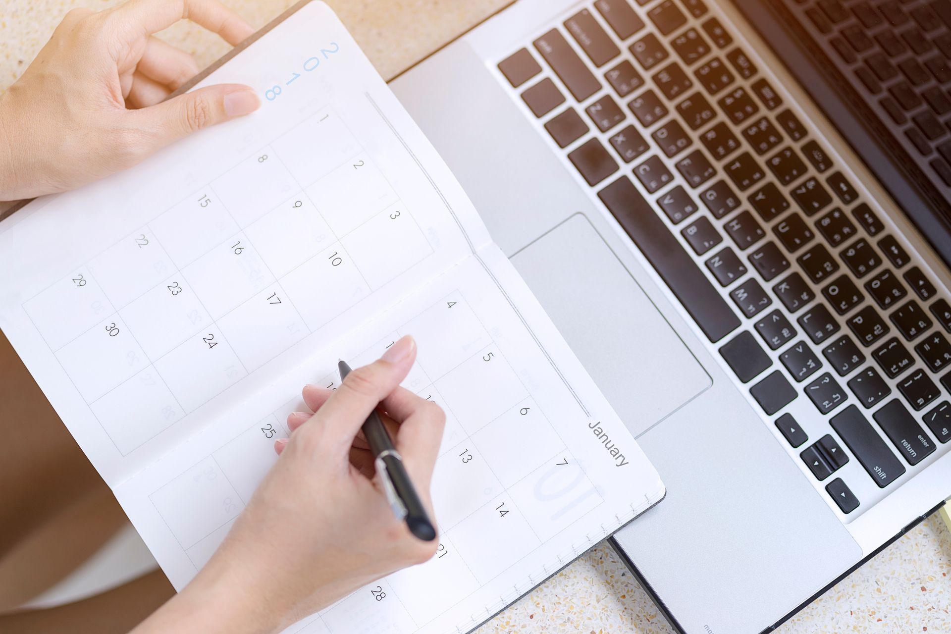Person writing in calendar, next to a laptop.
