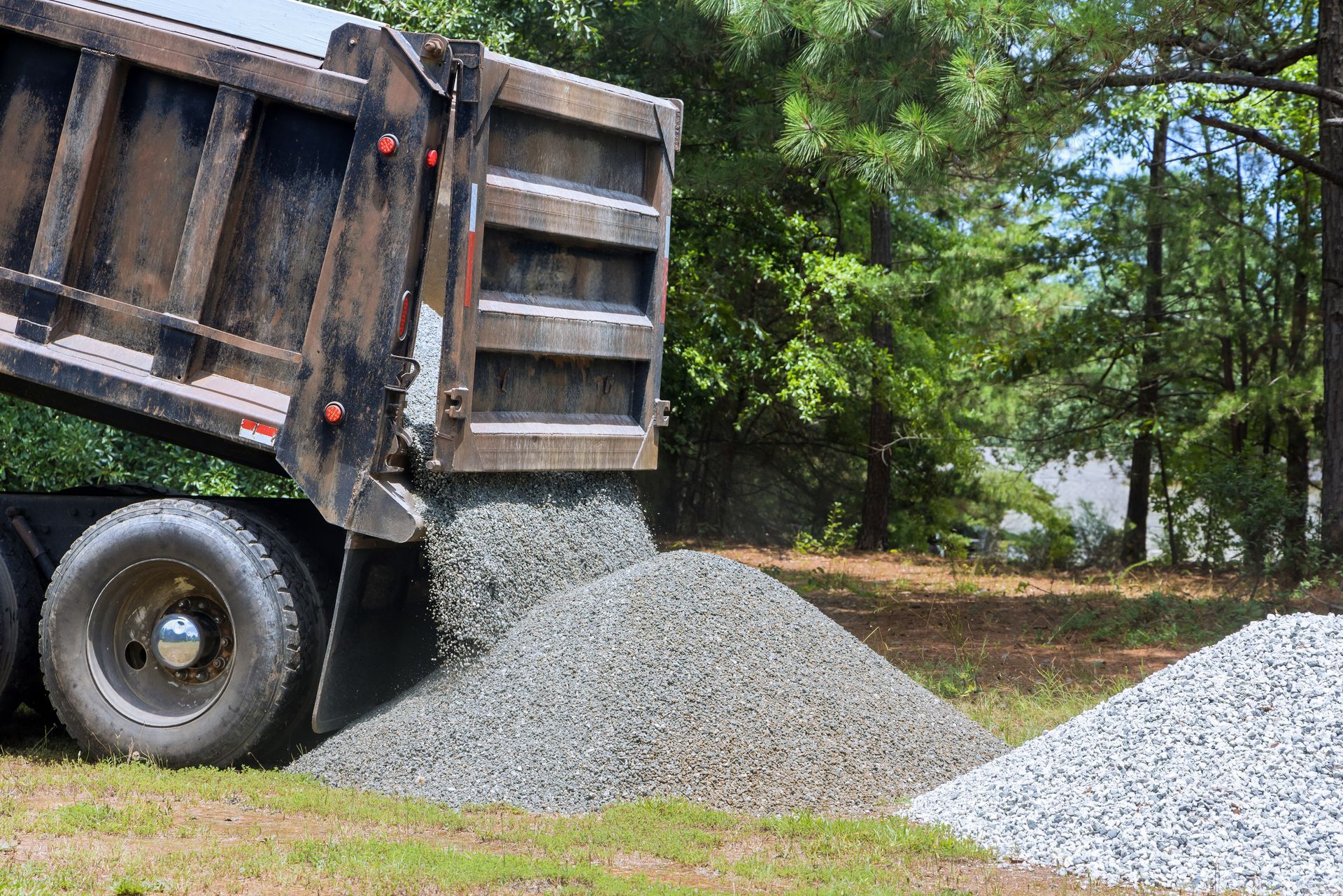A truck unloading gravel into a large pile at a worksite surrounded by trees.