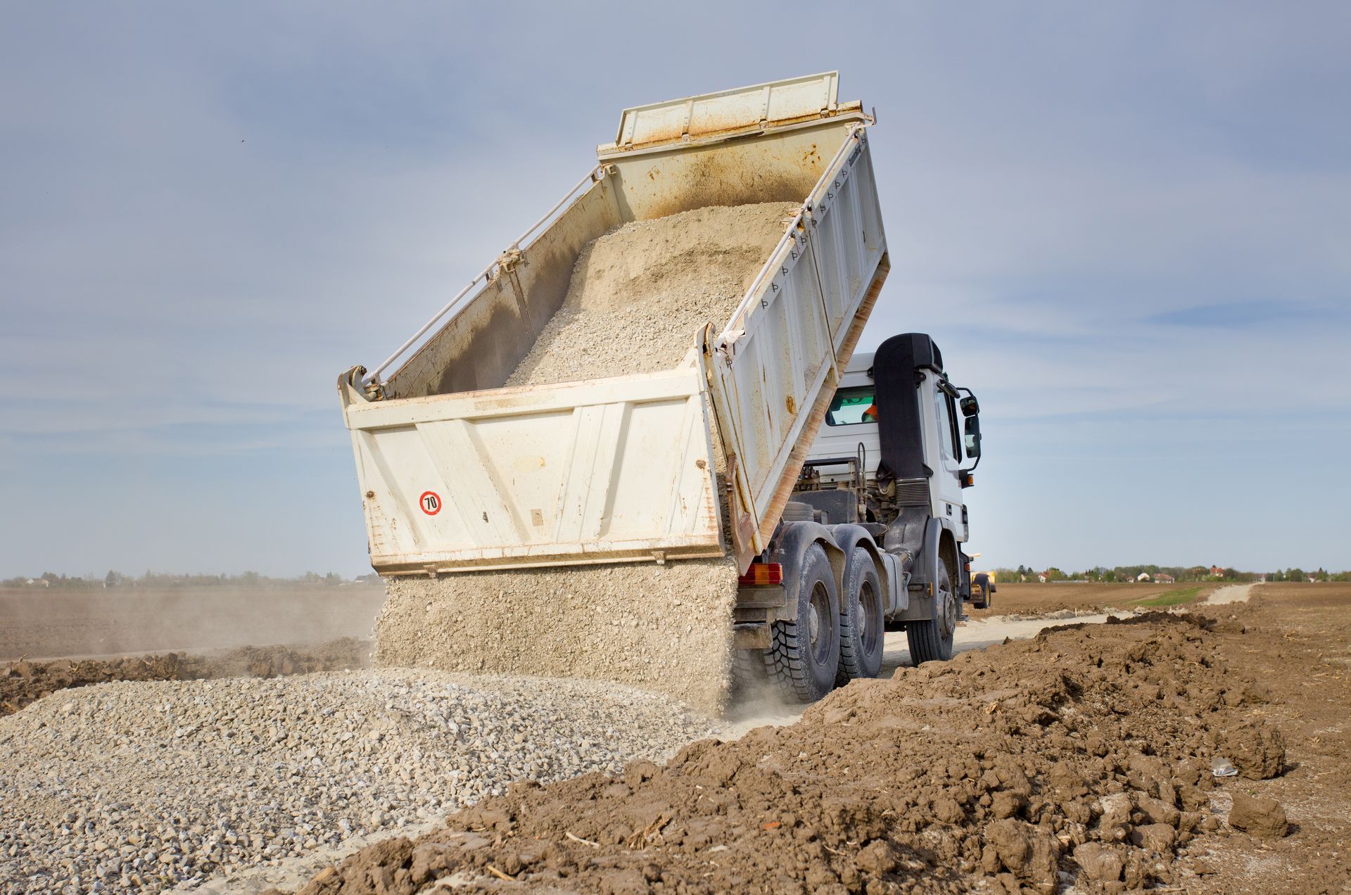 Dump truck unloading gravel on rural road construction site during aggregate delivery.