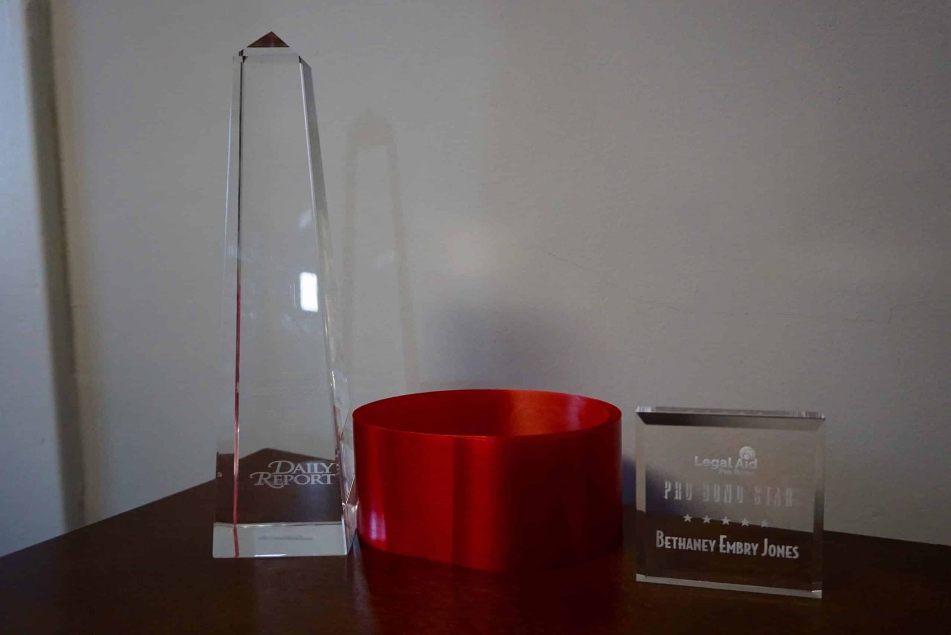 Three awards on a table: a tall clear glass trophy, a red bowl, and a small rectangular glass plaque.