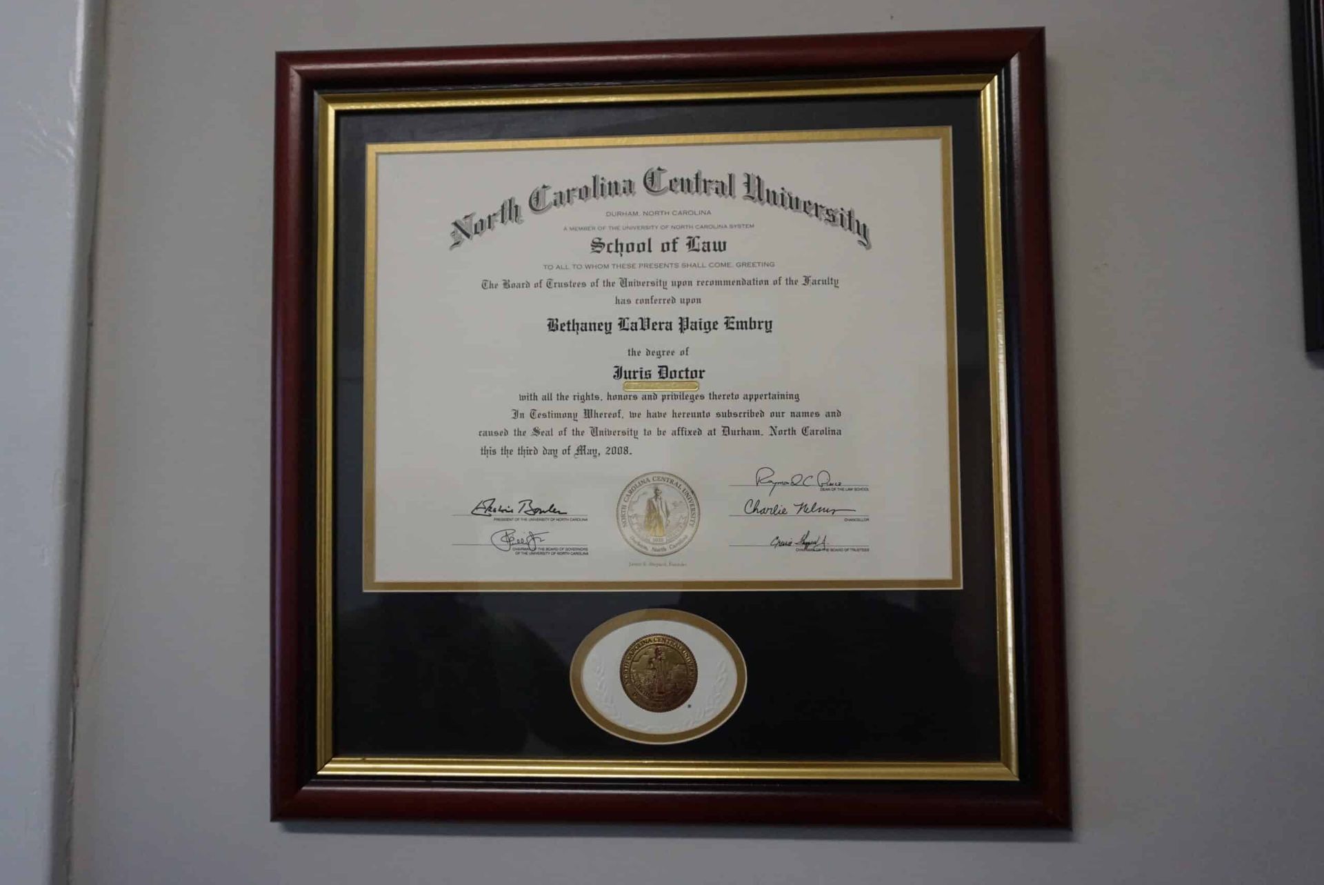 Framed certificate and seal on a wall in a dark wood and gold frame