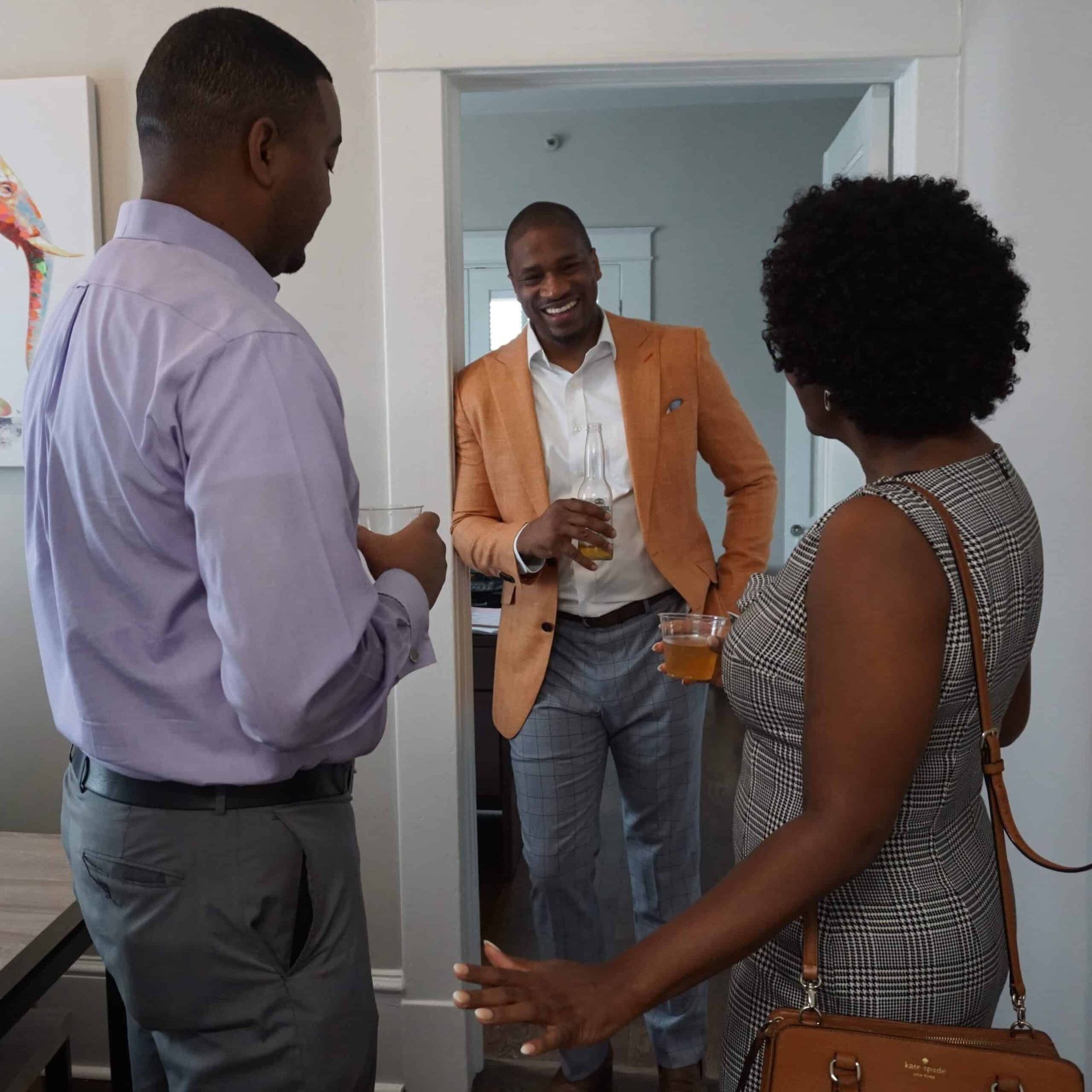Three people chatting in a doorway, one holding a drink and smiling.