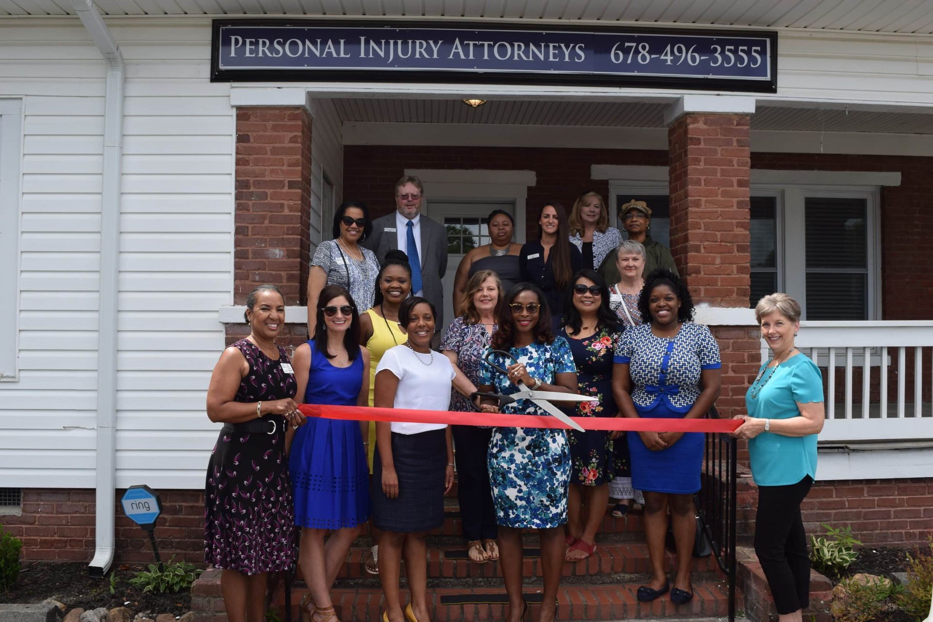 Group stands on a porch outside a personal injury attorneys office with a red ribbon across the entrance.