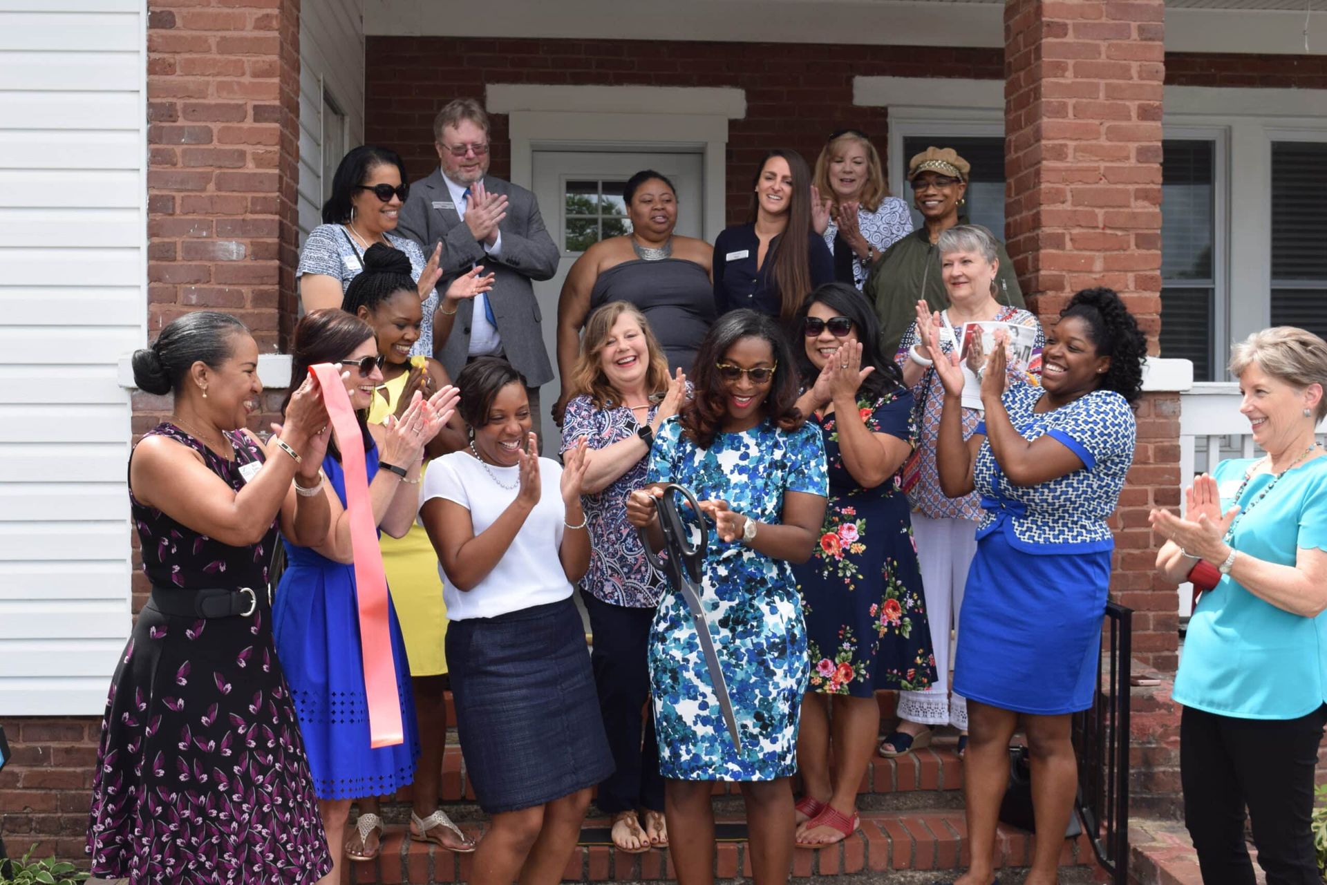 Group of people standing on porch, smiling and applauding at a house gathering
