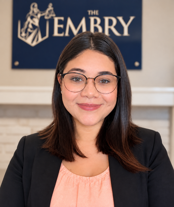Portrait of a smiling woman in glasses and blazer standing before The Embry sign