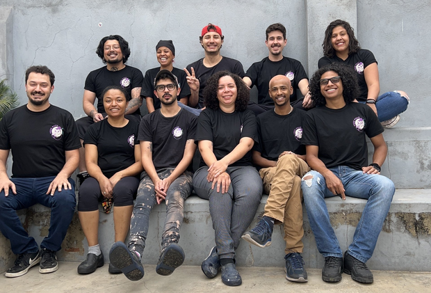 Grupo de pessoas diversas usando camisetas pretas sentadas do lado de fora sorrindo.