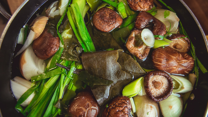Caldo de legumes com cogumelos, algas marinhas, cebolinha e fatias de cebola em uma panela.