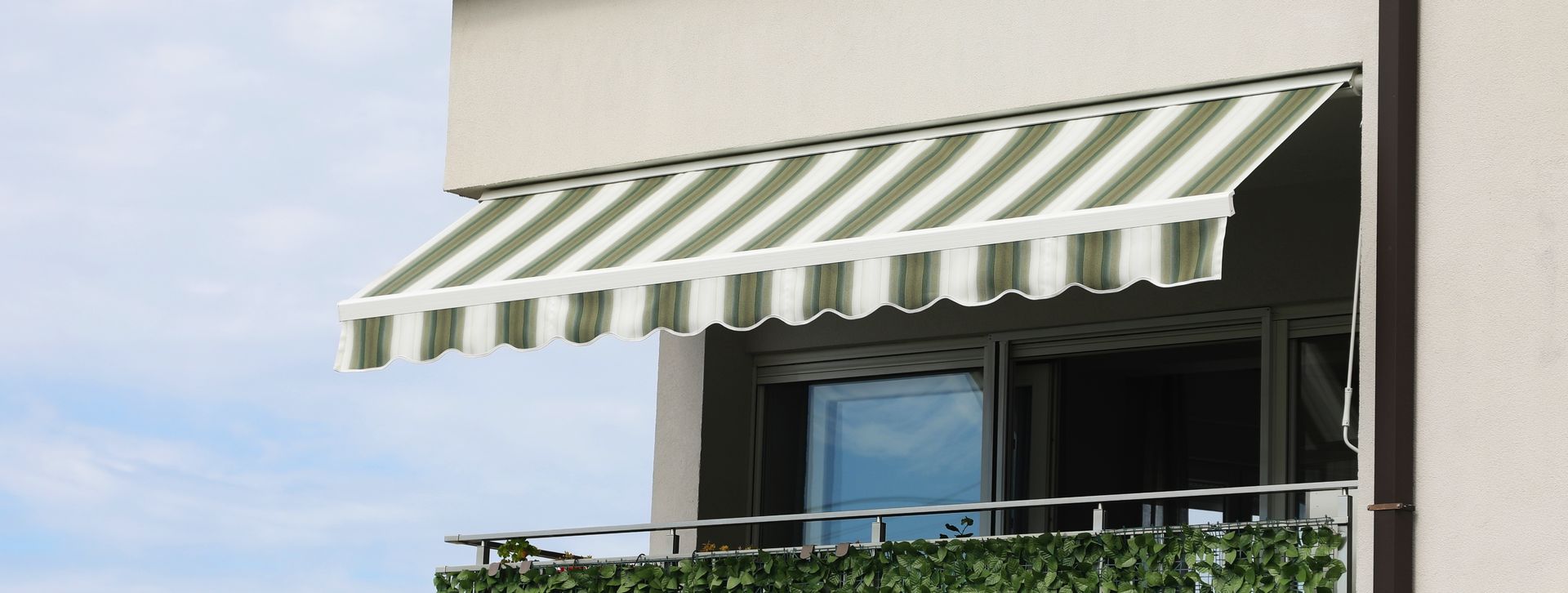 Retractable striped awning extending over a balcony on a residential building.