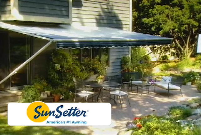 A gray house with a retractable awning over a patio set. The SunSetter logo is in the foreground.
