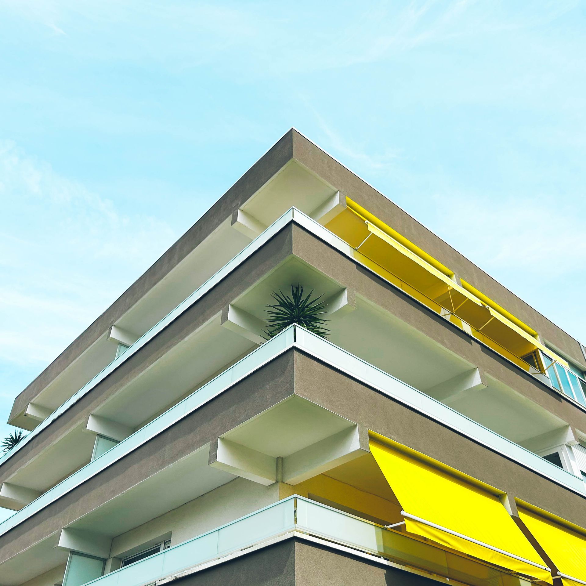 Modern apartment building with white balconies and yellow sunshades against a blue sky