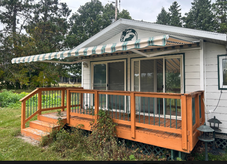 Small white house with an orange deck and awning, trees in the background.