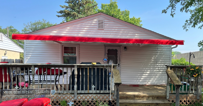 Red awning over a white-sided house with a deck; sunny day.