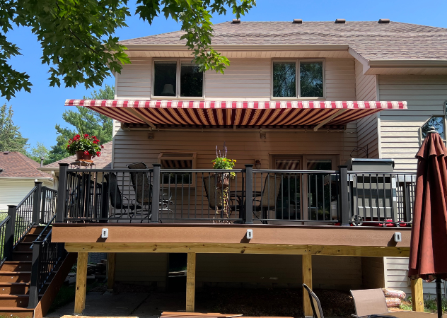 Deck with red and white striped awning, house, and deck furniture.