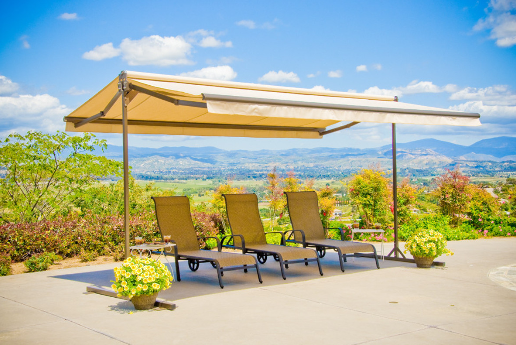 Three lounge chairs under a beige canopy, overlooking a scenic vista on a sunny day.