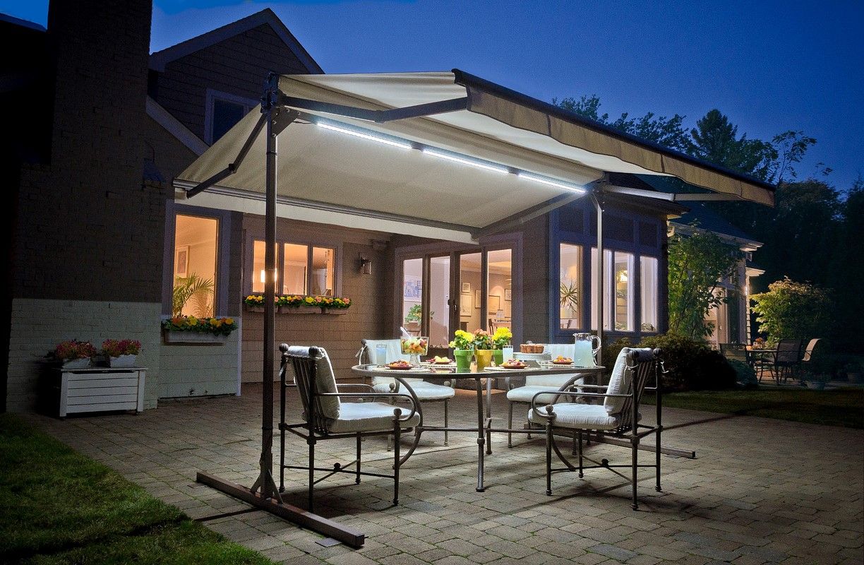 Patio dining set under illuminated beige awning at dusk.