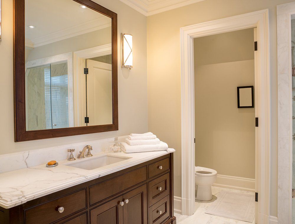 Bathroom with dark wood vanity, marble countertop, large mirror, and open doorway to a toilet room.