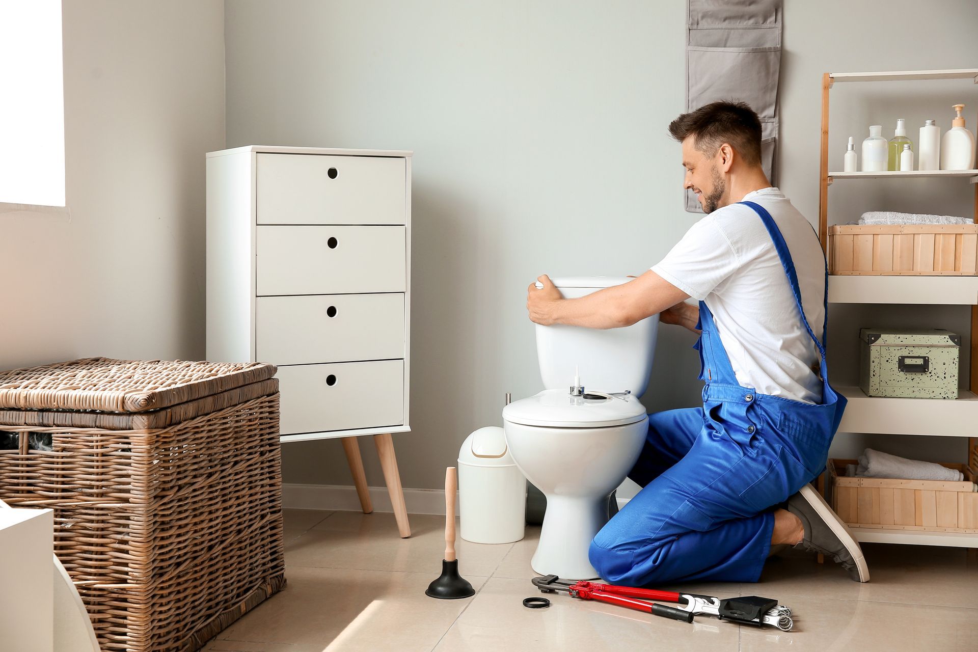 Plumber installing or repairing a toilet tank in a residential bathroom with plumbing tools nearby. Plumber installing or repairing a toilet tank in a residential bathroom with plumbing tools nearby.