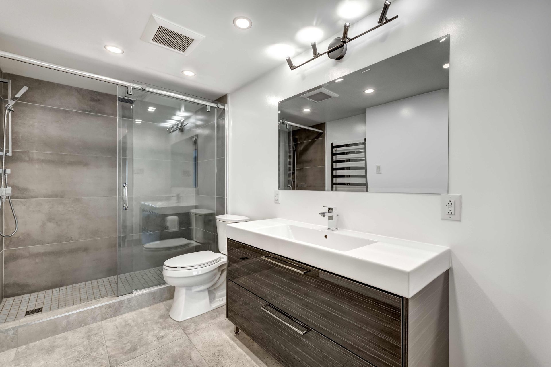 Modern bathroom with glass shower, large mirror, and sleek vanity.