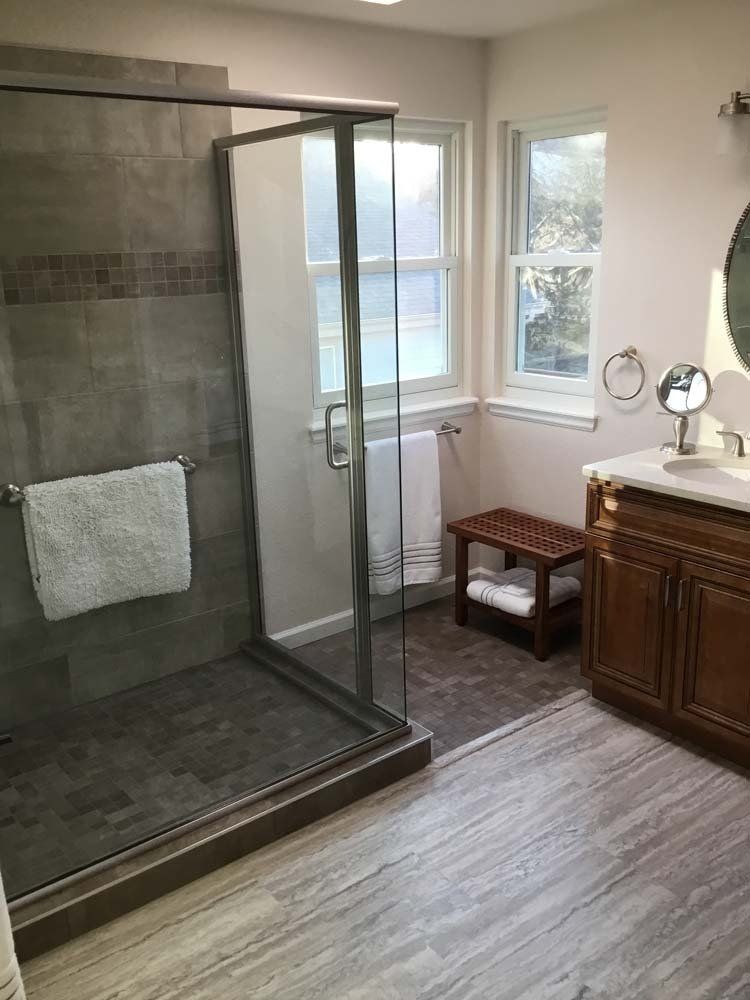 Bathroom with shower, vanity, and windows; gray tile, wooden cabinet, and neutral walls.