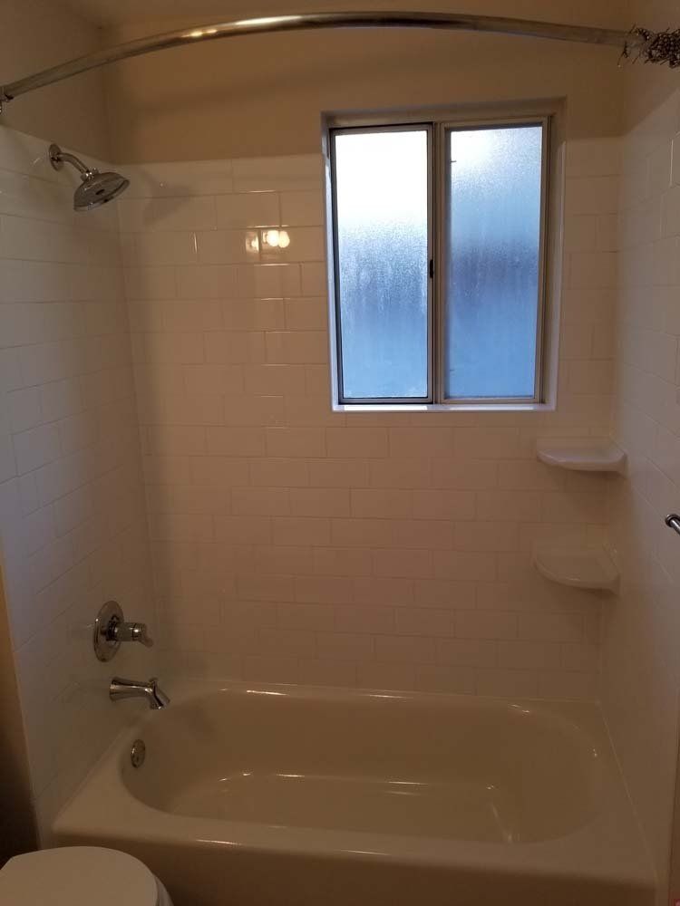 Bathroom with white tiled walls, bathtub, shower, and window.