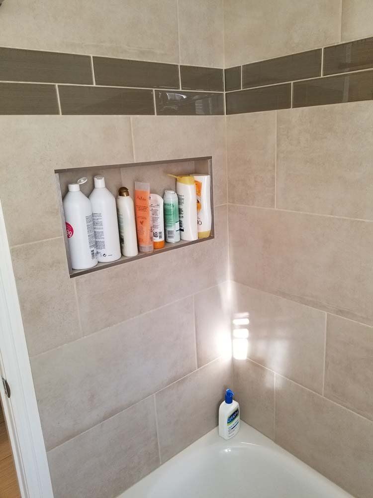 Bathroom shower with tile and built-in shelf holding toiletries.