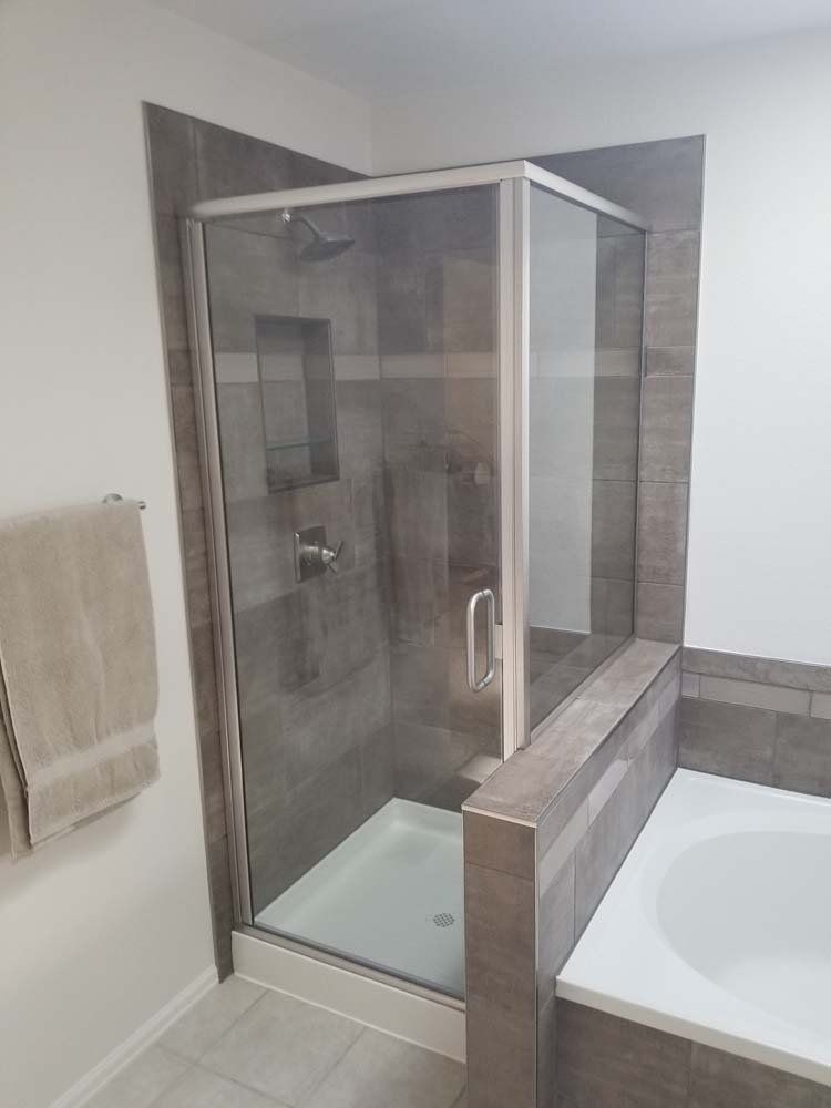 A modern bathroom with a glass shower enclosure and a built-in tub. Gray tiles and neutral tones.