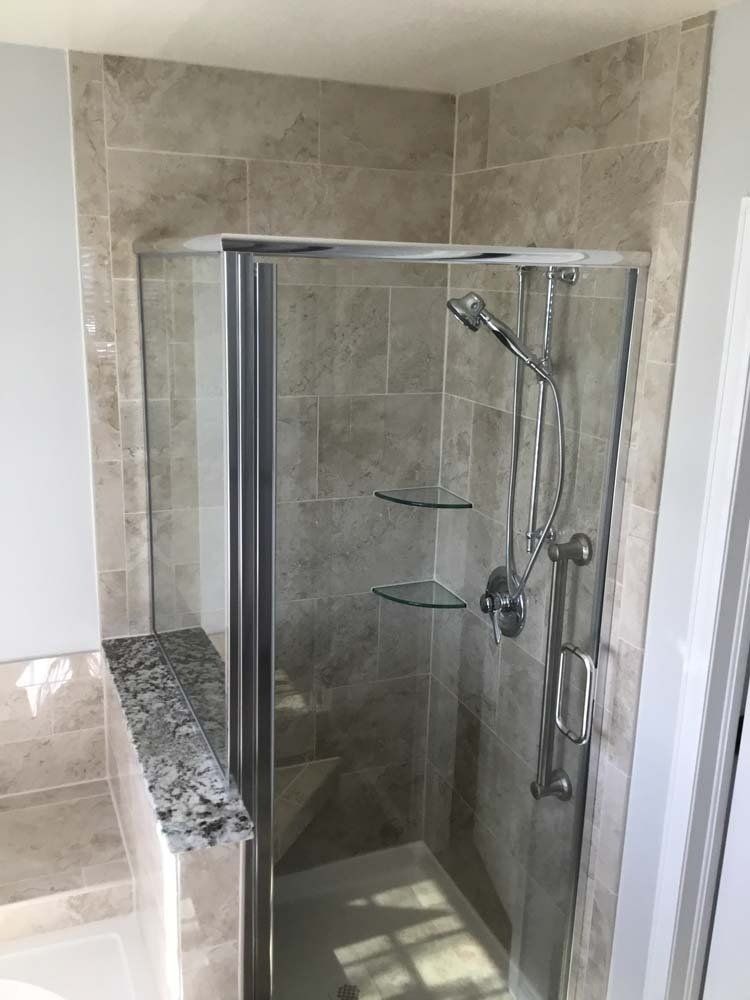 Shower stall with beige tile, glass door, silver fixtures, and granite ledge.