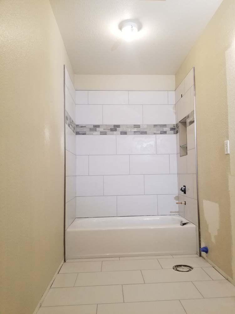 Bathroom with white tiles, bathtub, and neutral walls under a bright ceiling light.